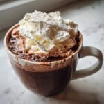 Close-up of a mug filled with rich Salted Maple Hot Chocolate, topped with whipped cream and flaky sea salt.