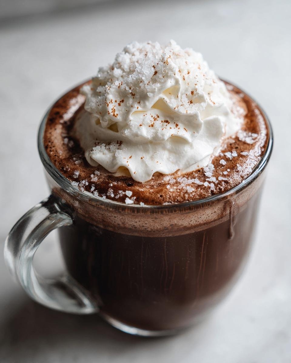 Close-up of a rich, dark Salted Maple Hot Chocolate topped with whipped cream and coarse sea salt.