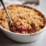 Close-up of a spoonful being taken from a baked Vegan Apple Cranberry Crisp showing the bubbly fruit filling and crisp topping.