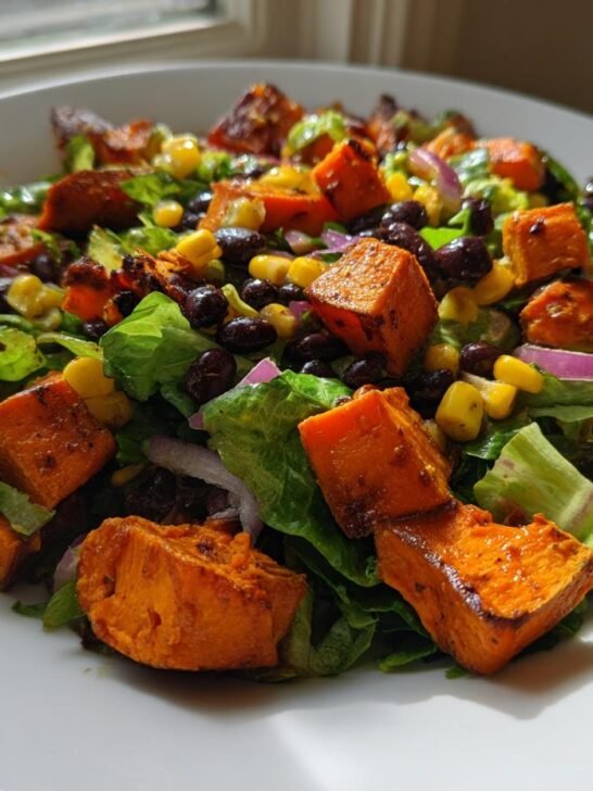 Close-up of a vibrant Spicy Chipotle Sweet Potato Chopped Salad featuring roasted sweet potatoes, black beans, corn, and red onion over lettuce.