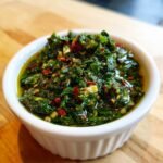 A close-up of My Staple Chimichurri Sauce, bright green and oily, in a small white ramekin.