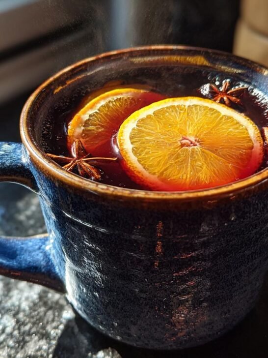 Close-up of a steaming Spiced Apple Cider Mocktail in a blue mug, garnished with orange slices and star anise.