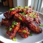 A pile of glistening Sticky Gochujang Chicken Wings coated in sauce, topped with sesame seeds and green onions.