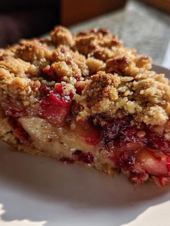 Close-up of a slice of Vegan Apple Cranberry Crumble Pie showing the thick, golden crumble topping and juicy fruit filling.