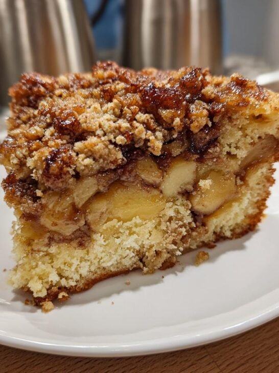 A moist slice of Vegan Apple Crumble Coffee Cake showing layers of cake, spiced apples, and a crunchy brown sugar topping.