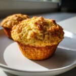 Close-up of a golden-brown Vegan Chai Spice Muffin with a crumbly, spiced top, sitting on a white plate.