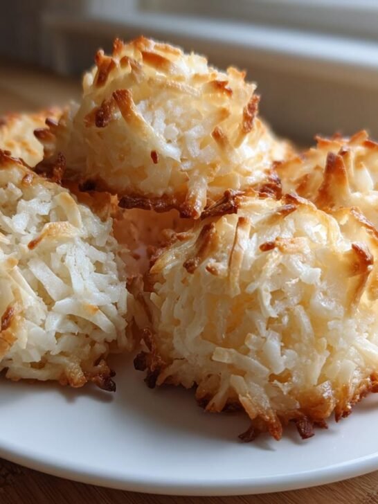 A close-up of several golden-brown Vegan Coconut Macaroons piled on a small white plate.