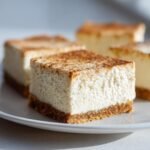 Close-up of creamy Vegan Eggnog Cheesecake Bars with a graham cracker crust, dusted with cinnamon.