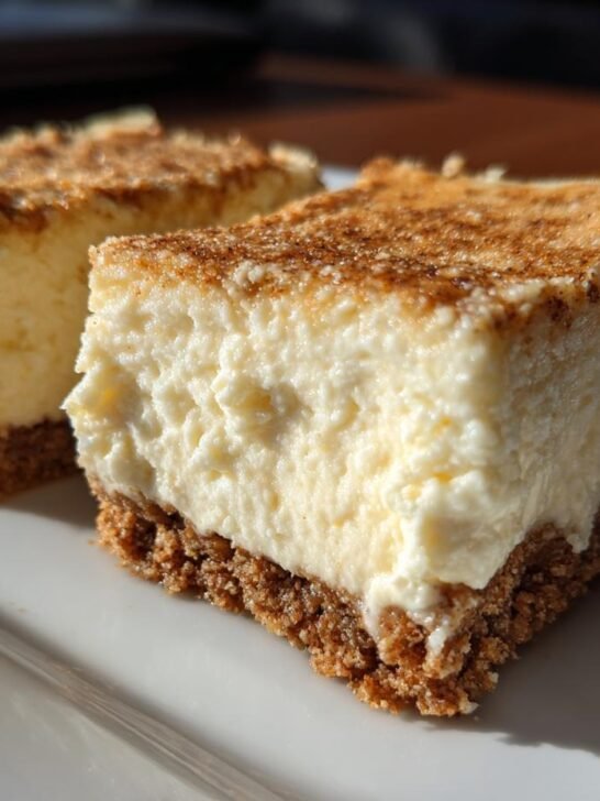 Two squares of creamy Vegan Eggnog Cheesecake Bars with a graham cracker crust and cinnamon dusting.