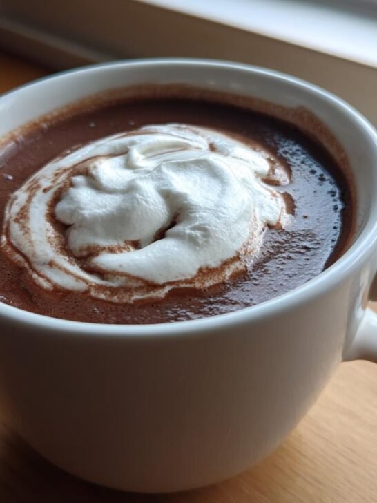Close-up of a mug of rich Vegan Hot Cocoa With Coconut Cream, topped with a swirl of white cream.
