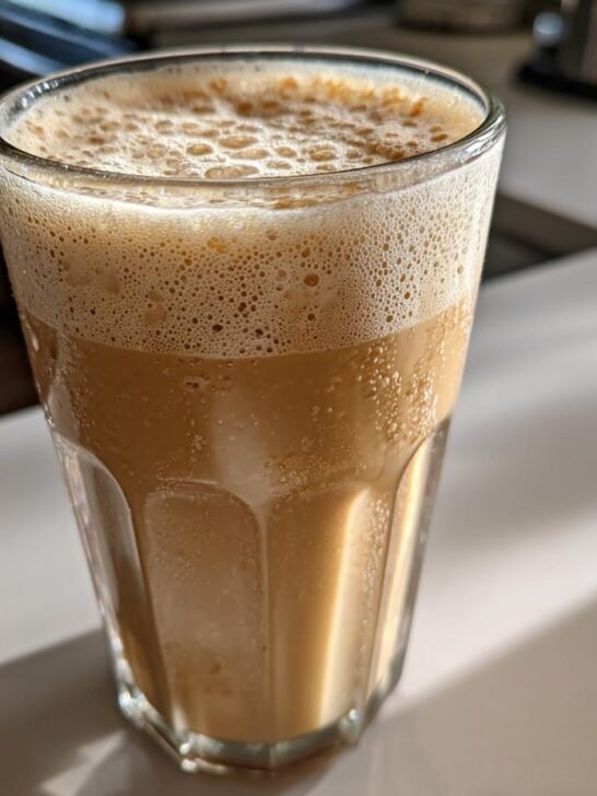 A tall, ribbed glass filled with a creamy, light brown Vegan Jamaican Irish Moss Sea Moss Drink topped with thick foam.