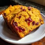 Close-up of two thick slices of golden Vegan Orange Cranberry Bread studded with bright red dried cranberries.