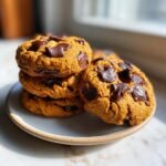 A stack of soft Vegan Pumpkin Chocolate Chip Cookies loaded with melted dark chocolate chunks on a small plate.