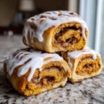 Three stacked Vegan Pumpkin Pie Cinnamon Rolls generously topped with white glaze icing.