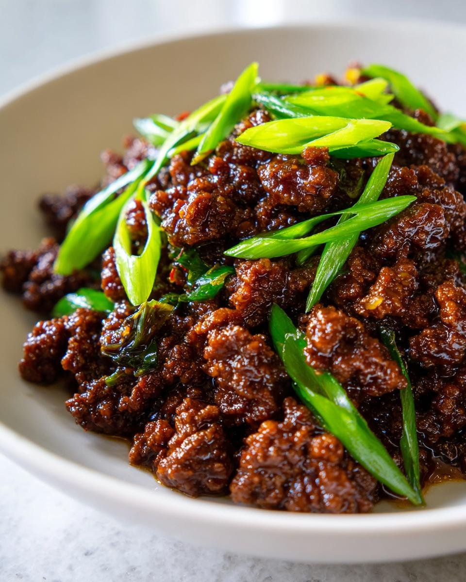 A close-up of glistening, saucy Asian ground beef topped generously with bright green sliced scallions.