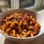 A close-up of a white bowl filled with American Chop Suey, featuring elbow macaroni and rich meat sauce.