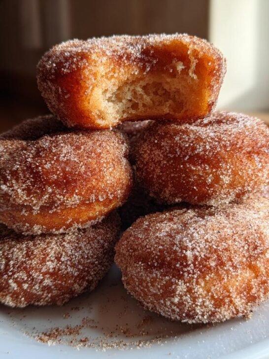 A stack of freshly made, sugar-coated Apple Cider Donuts Recipe, with one donut on top showing a bite taken out.