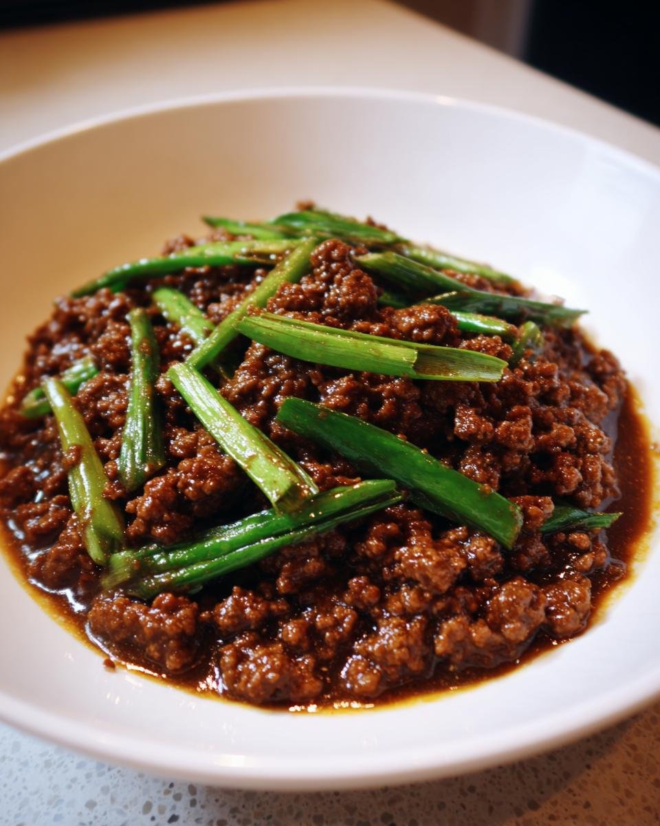 A close-up of rich, saucy Asian ground beef topped with bright green scallions in a white bowl.