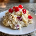 A scoop of creamy Banana Split Fluff Salad topped with bright red maraschino cherries and banana slices.