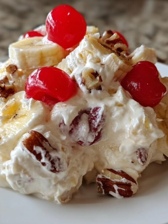 A scoop of creamy Banana Split Fluff Salad topped with banana slices, pecans, and bright red maraschino cherries.