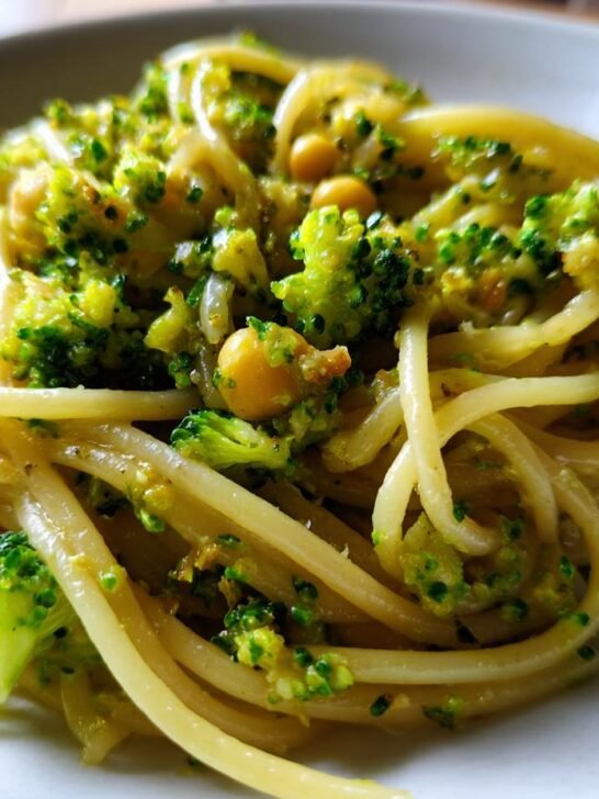 Close-up of spaghetti tossed with bright green broccoli florets and chickpeas in a garlic olive oil sauce.