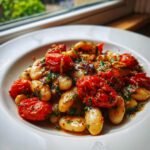 Close-up of Burst Tomato Basil Butter Beans served in a white bowl near a window.