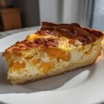 A golden-brown slice of Butternut Squash Quiche resting on a white plate, showing chunks of orange squash in the creamy filling.
