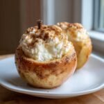 Close-up of a baked apple filled high with creamy cheesecake filling and dusted with cinnamon, one of the Cheesecake Stuffed Baked Apples.