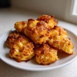 A pile of golden brown Cheesy Baked Cauliflower Tots with crispy, melted cheese topping on a white plate.