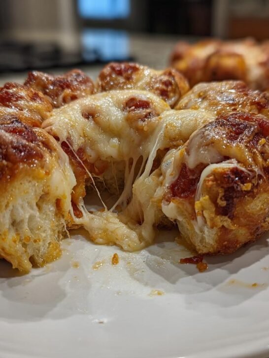 Close-up of a serving of Pizza Monkey Bread with melted, stringy cheese pulling apart, sitting on a white plate.
