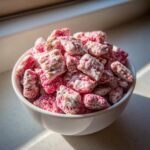 A white bowl filled with bright pink and white coated Cherry Cheesecake Puppy Chow cereal pieces.
