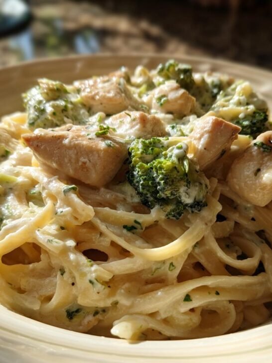 Close-up of creamy Chicken Alfredo With Broccoli tossed with fettuccine pasta in a light-colored bowl.