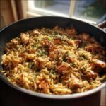 Close-up of seasoned Chicken And Orzo mixed together in a dark skillet, garnished with fresh parsley.