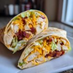 A close-up of a halved Chicken Bacon Ranch Wrap showing chunks of chicken, bacon, shredded cheese, and lettuce.