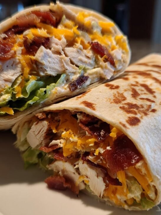 Two halves of a toasted Chicken Bacon Ranch Wrap showing filling of chicken, bacon, cheese, and lettuce.