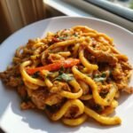 A close-up of creamy Chicken Fajita Pasta featuring thick noodles, seasoned chicken, and red bell peppers, garnished with herbs.