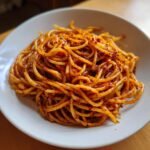 A close-up, appetizing shot of glossy spaghetti tossed in vibrant red chili oil, showcasing the texture of the Chili Oil Pasta.
