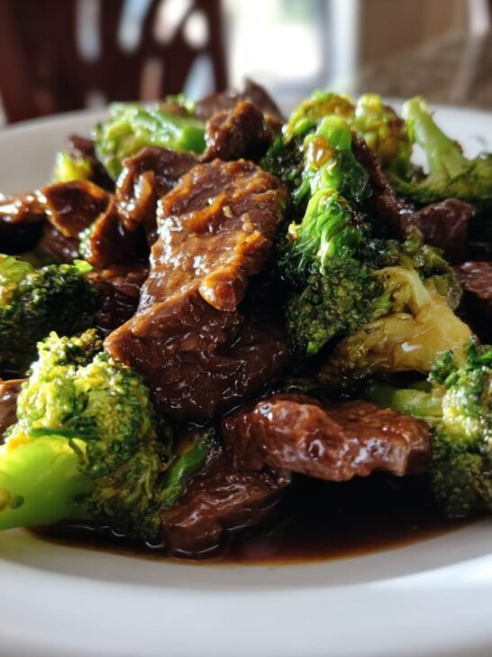 A close-up shot of tender slices of beef mixed with bright green broccoli florets coated in savory sauce for Chinese Beef And Broccoli.