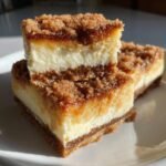 Close-up of stacked Churro Cheesecake bars showing a creamy white layer and a cinnamon-sugar crumble topping.