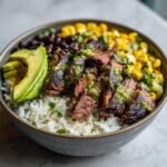 Close-up of a Cilantro Lime Steak Bowls featuring sliced steak over rice, topped with avocado, corn, and black beans.