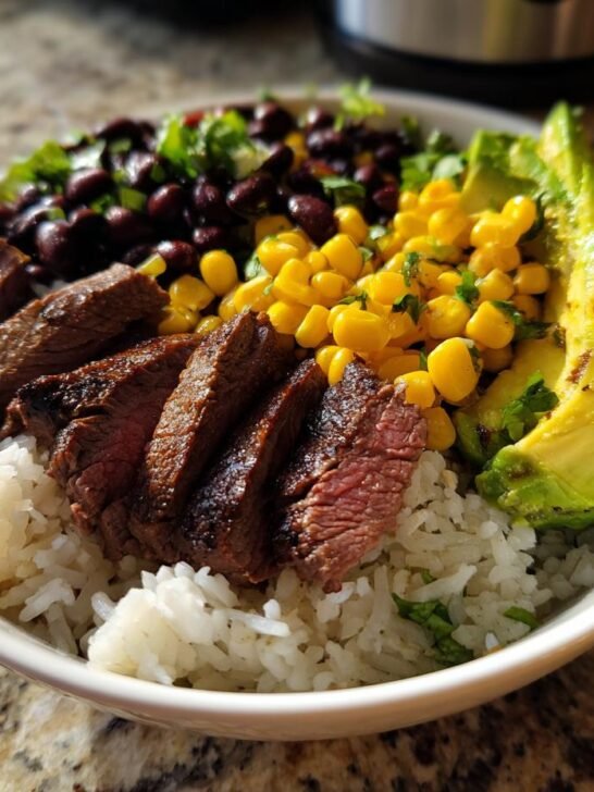 A close-up of a Cilantro Lime Steak Bowls featuring sliced steak over rice, corn, black beans, and avocado.
