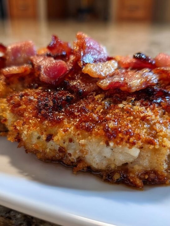 Close-up of a crispy, breaded Country Fried Pork Chops Bacon served on a white plate with rendered juices.
