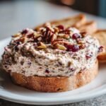 A thick spread of Cranberry Cream Cheese Dip topped with pecans and dried cranberries served on toasted bread.