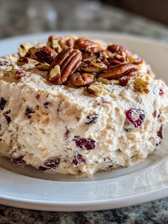 A mound of Cranberry Cream Cheese Dip mixed with dried cranberries and topped with whole and chopped pecans on a white plate.