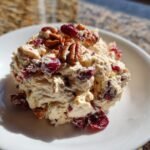 A scoop of creamy Cranberry Pecan Chicken Salad topped with whole pecans and dried cranberries on a white plate.