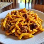 Close-up of a white bowl filled with Creamy Butternut Squash Pasta With Sausage, featuring thick pasta coated in orange sauce and chunks of browned sausage.