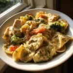 A close-up bowl of Creamy Chicken Tortellini With Veggies, featuring pasta, chicken chunks, broccoli, and carrots in a rich sauce.
