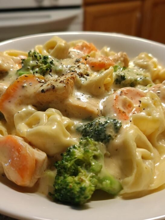 A close-up of Creamy Chicken Tortellini With Veggies coated in a rich sauce, served in a white bowl.