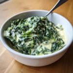 A white bowl filled with creamy, cooked frozen spinach, ready to eat with a spoon.