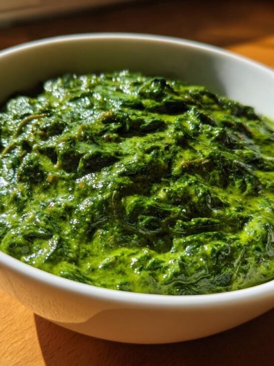 Close-up of rich, creamy cooked Frozen Spinach served in a small white bowl on a wooden surface.